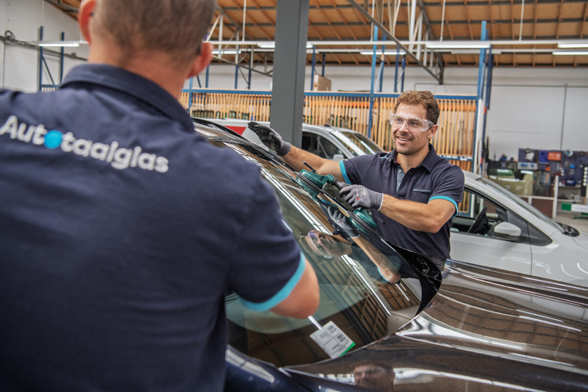Twee monteurs van Autotaalglas plaatsen vakkundig een nieuwe autoruit in een auto en zorgen voor een veilige, perfect passende voorruitvervanging.